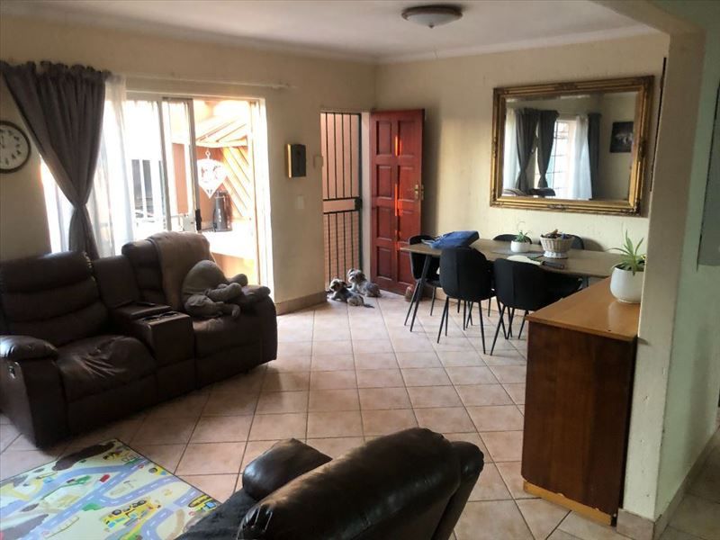 Open-plan living and dining area featuring tiled flooring, a security gate, and sliding door access to the outdoor space.