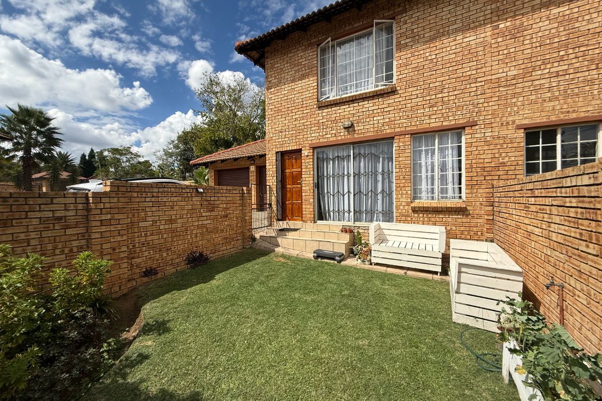 Rear view of a face brick townhouse featuring a private garden, lawn area, and sliding door access to the main living space.