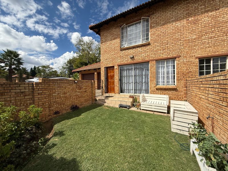 Rear view of a face brick townhouse featuring a private garden, lawn area, and sliding door access to the main living space.