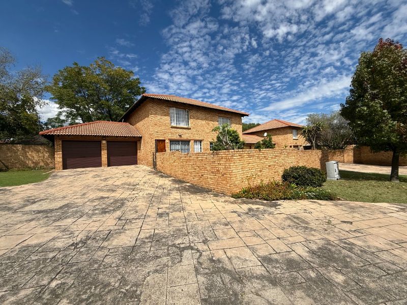 Front view of a facebrick townhouse featuring a double garage, paved driveway, and perimeter boundary wall under a clear sky.