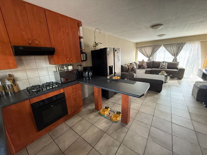 Open-plan living area featuring a kitchen with wood-finish cabinetry, gas hob, and tiled flooring, seamlessly flowing into the adjacent lounge space.