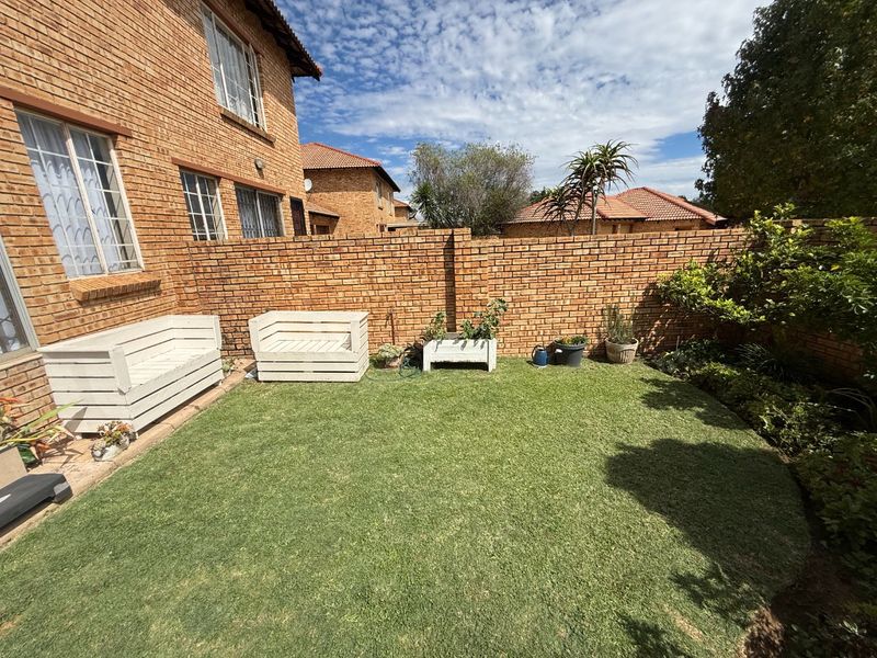 A private rear garden area featuring a well-maintained lawn, enclosed by a face brick perimeter wall and adjacent to the townhouse structure.