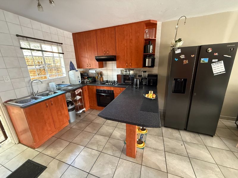Functional kitchen featuring wooden cabinetry, laminate countertops, built-in oven with gas hob, and a breakfast bar, finished with tiled flooring and splashbacks.