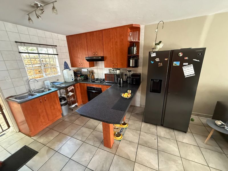 Functional kitchen featuring wood-look cabinetry, a breakfast bar, built-in oven with gas hob, and tiled flooring throughout.