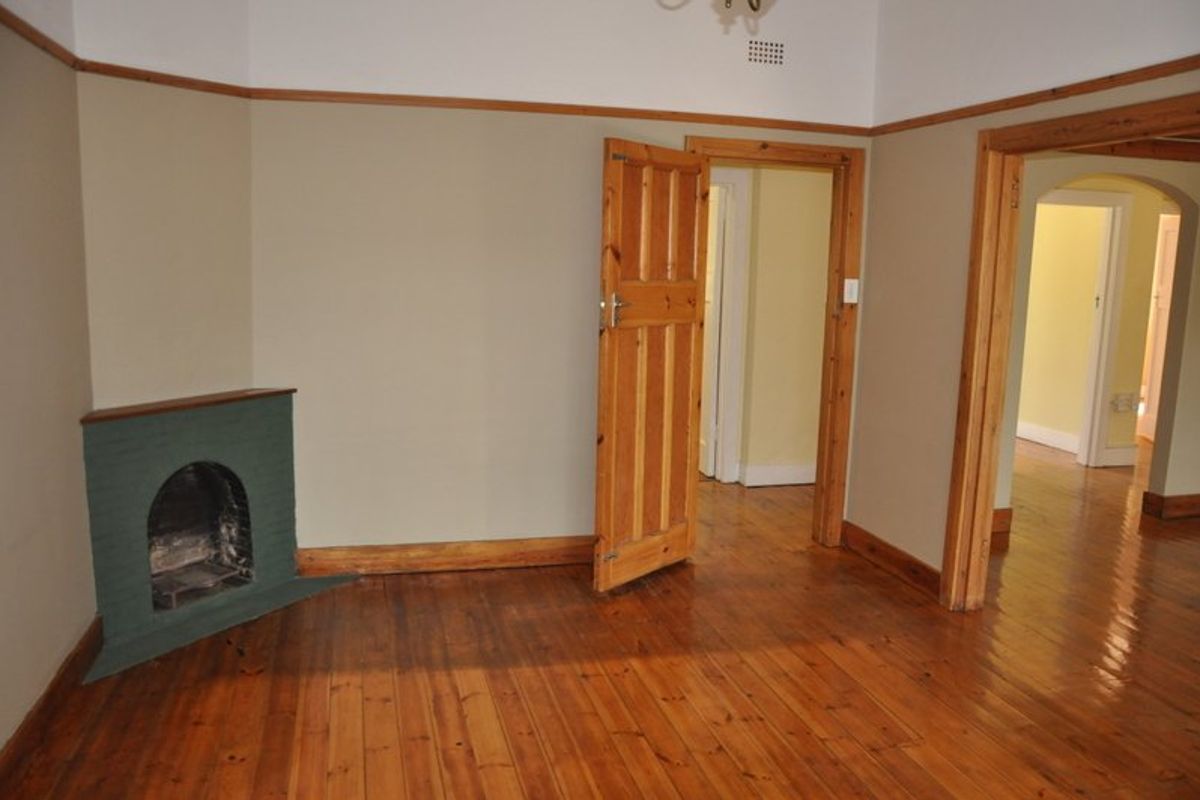 An empty living room featuring polished timber flooring, a corner fireplace, and classic timber door frames with a picture rail.