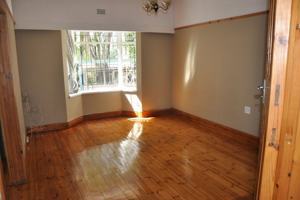 An empty bedroom featuring polished timber flooring, a bay window with security bars, and classic timber trim details.