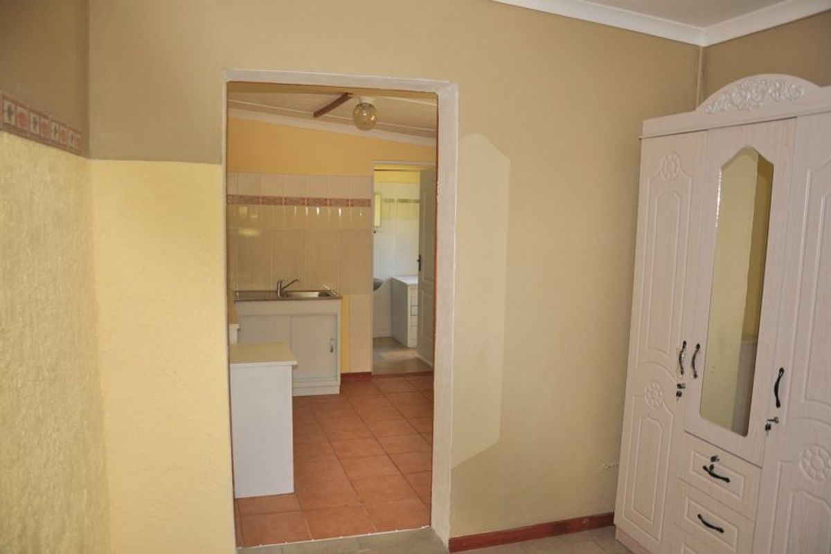 A view through a doorway into a functional kitchen area featuring tiled flooring and a basic sink unit with tiled splashbacks.