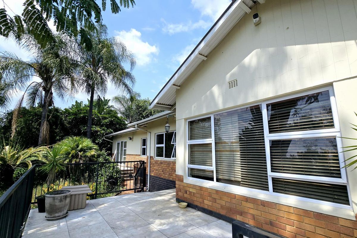 A rear exterior view of the house featuring a tiled patio area, brick and painted wall finishes, and aluminium window frames.