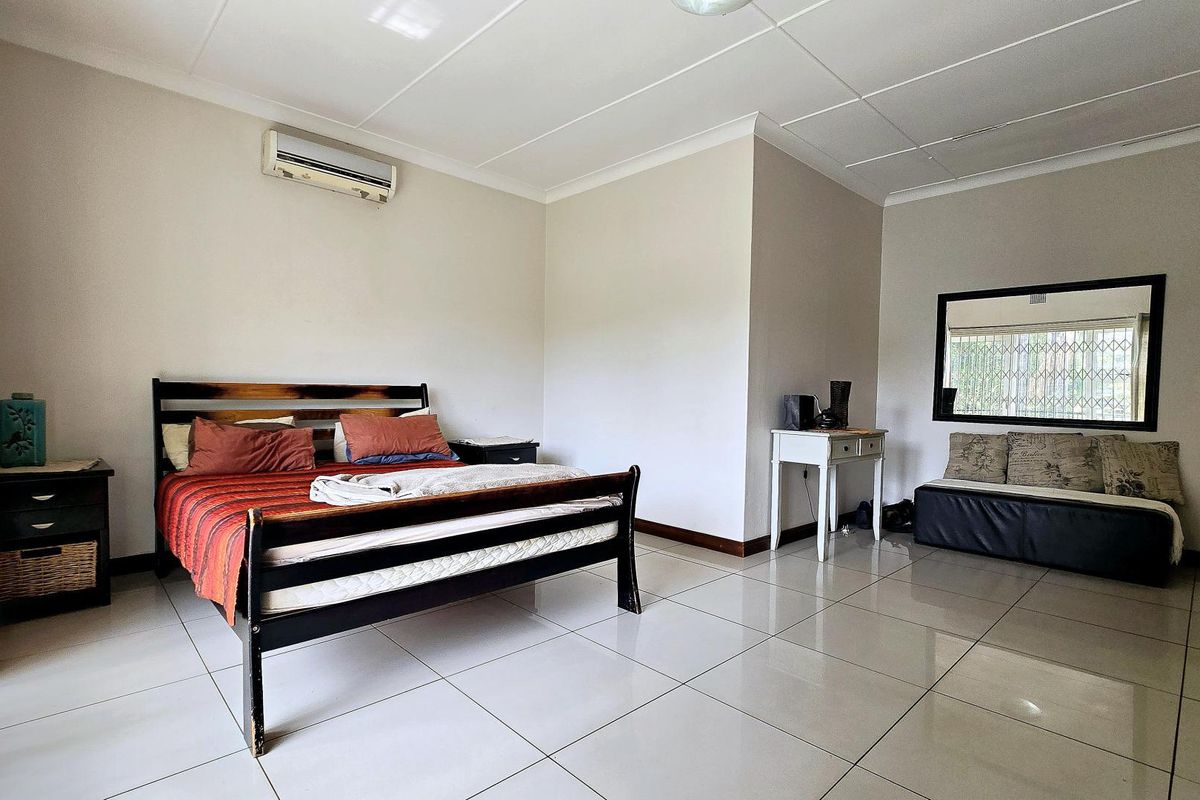 Spacious bedroom featuring neutral walls, large format floor tiles, a split-system air conditioner, and a window fitted with a security gate.