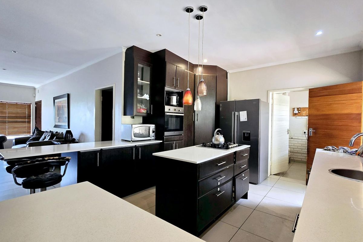 Spacious open-plan kitchen featuring a central island, modern dark cabinetry, stone countertops, and integrated appliances, flowing into the adjacent living area.