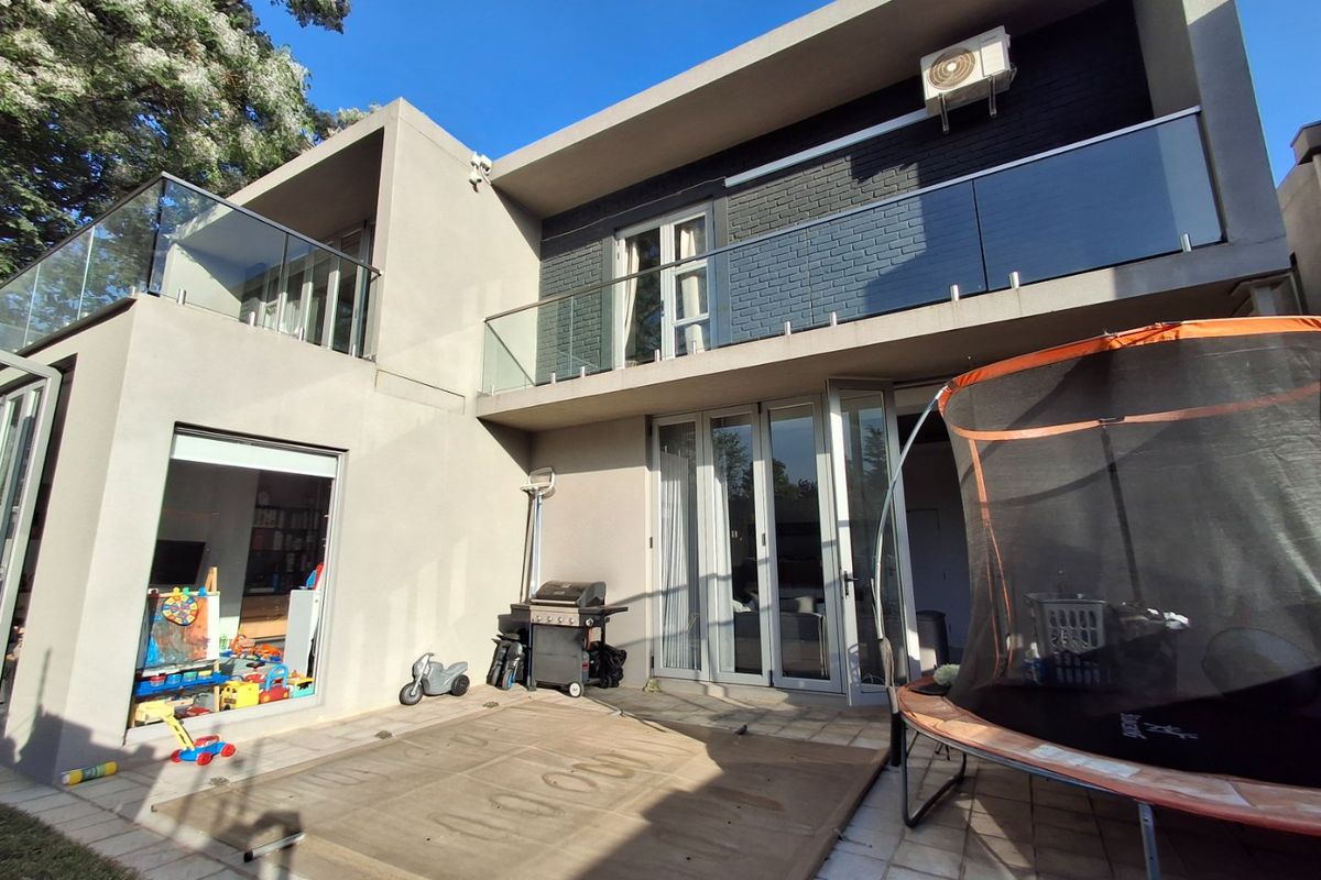 Rear view of a modern townhouse featuring a paved patio, bi-fold doors, and upper-level balconies with glass balustrades.