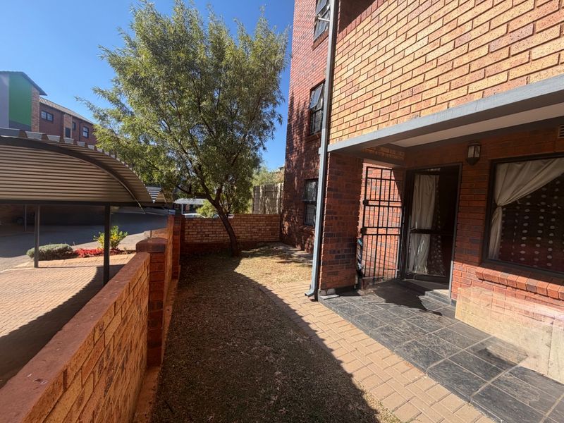 A private rear courtyard featuring a paved patio area, face brick exterior walls, and a small garden space with a security gate entrance.
