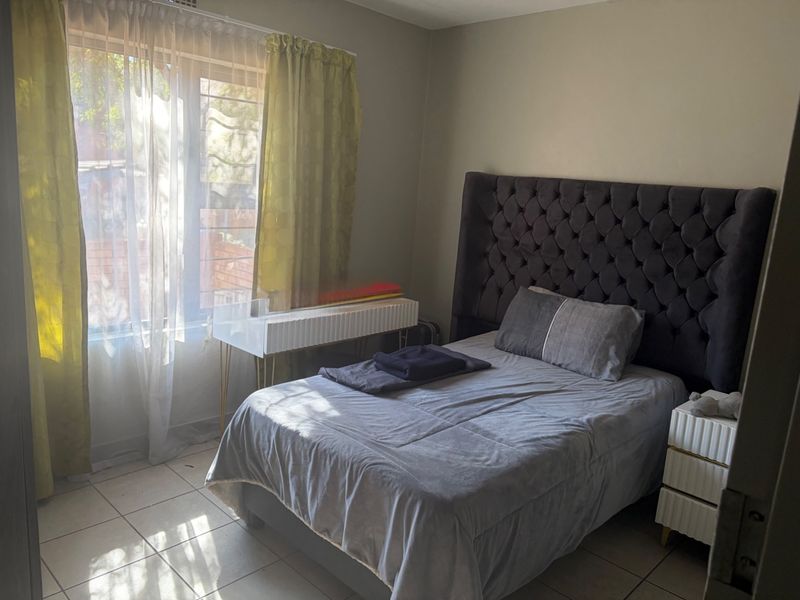A bedroom featuring tiled flooring and a window with security bars, providing natural light.