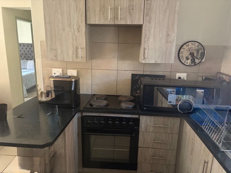 Compact kitchen featuring light wood-grain cabinetry, black granite countertops, a built-in electric oven and hob, and neutral tiled backsplash.