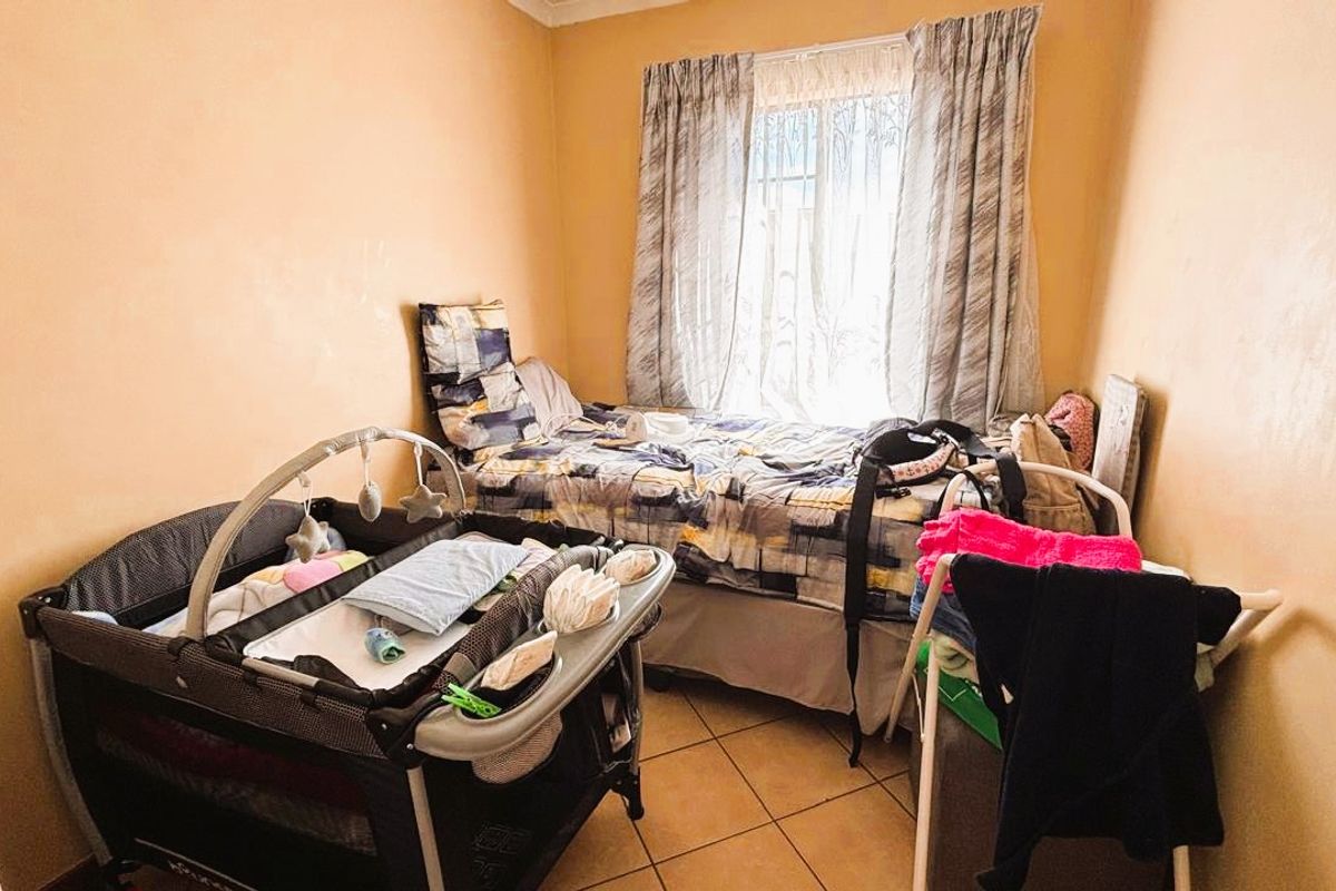 A compact bedroom featuring tiled flooring and a window, currently utilized as a nursery and sleeping space.