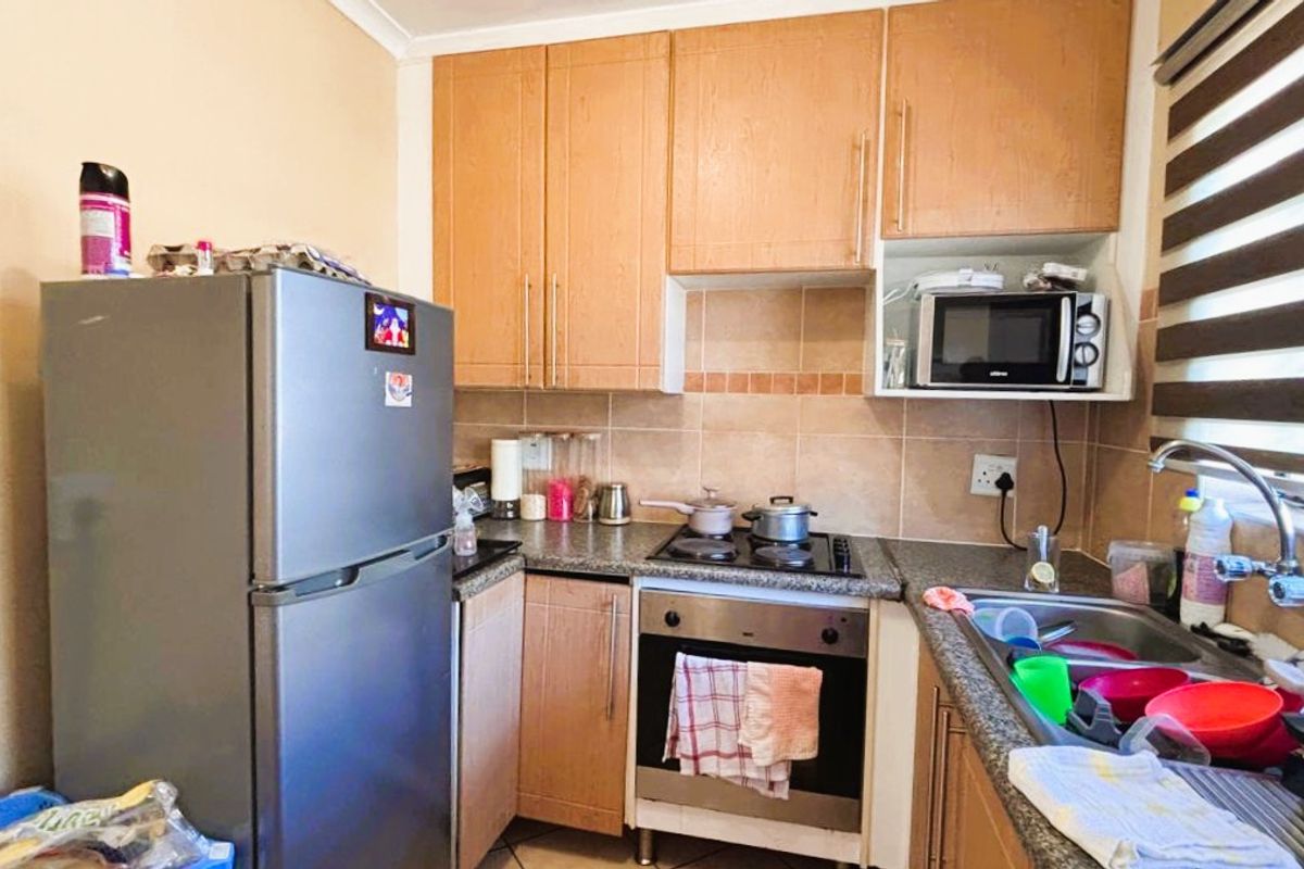 Compact kitchen featuring light wood cabinetry, granite countertops, a built-in oven with hob, and a tiled backsplash.