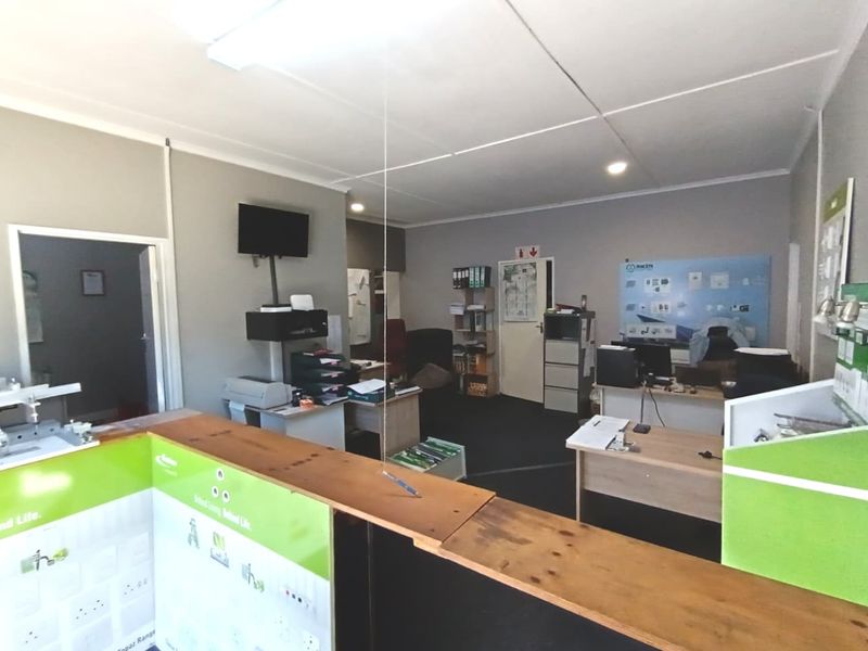 A functional commercial office space featuring a reception counter, suspended ceiling with recessed lighting, and multiple workstations in an open-plan layout.