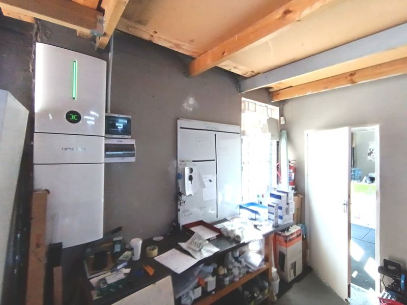 A functional utility space featuring an installed solar inverter, electrical distribution board, and exposed timber ceiling beams, suitable for storage or technical operations.