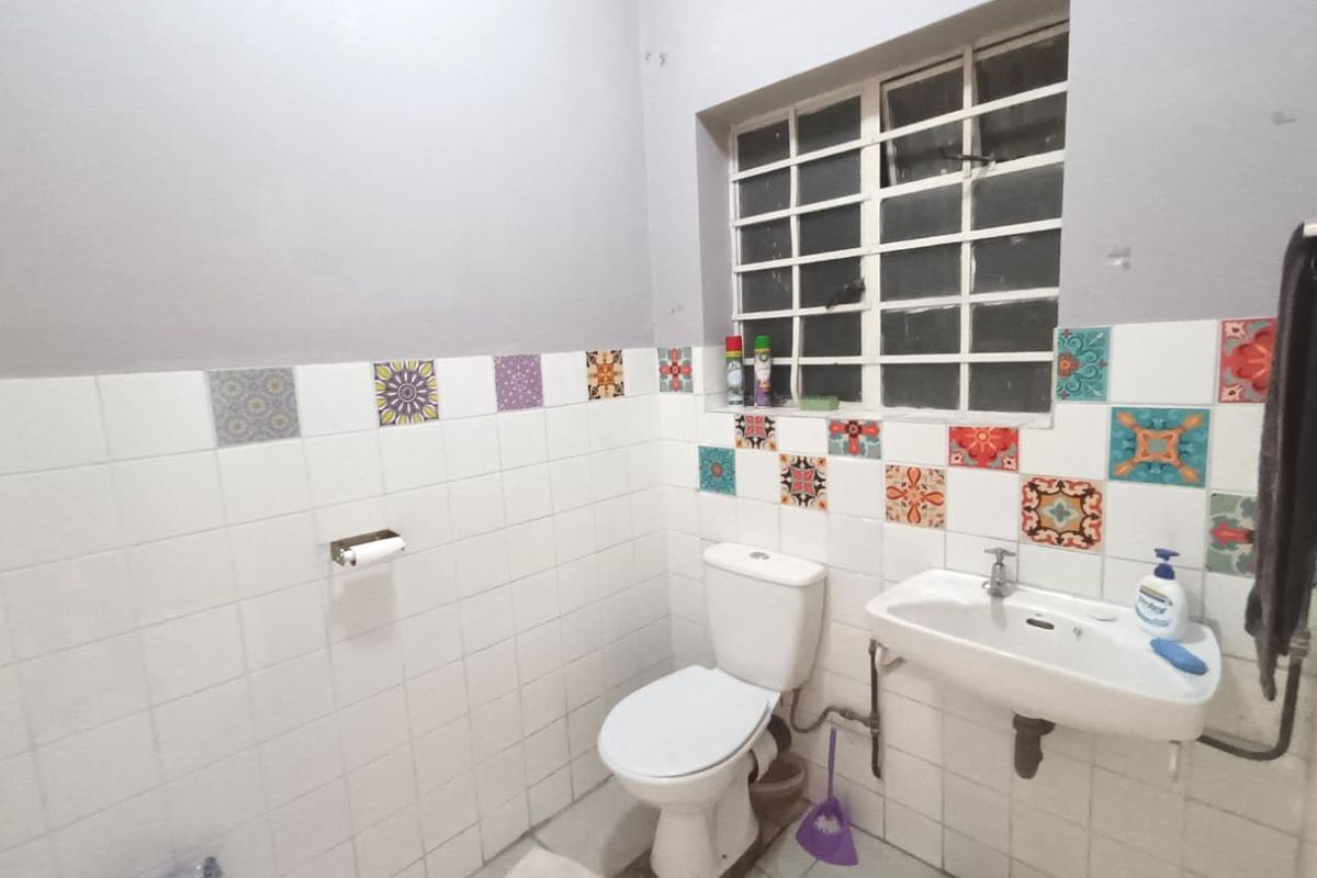 A functional bathroom featuring a wall-mounted basin, toilet, and decorative tiled walls with security bars on the window.