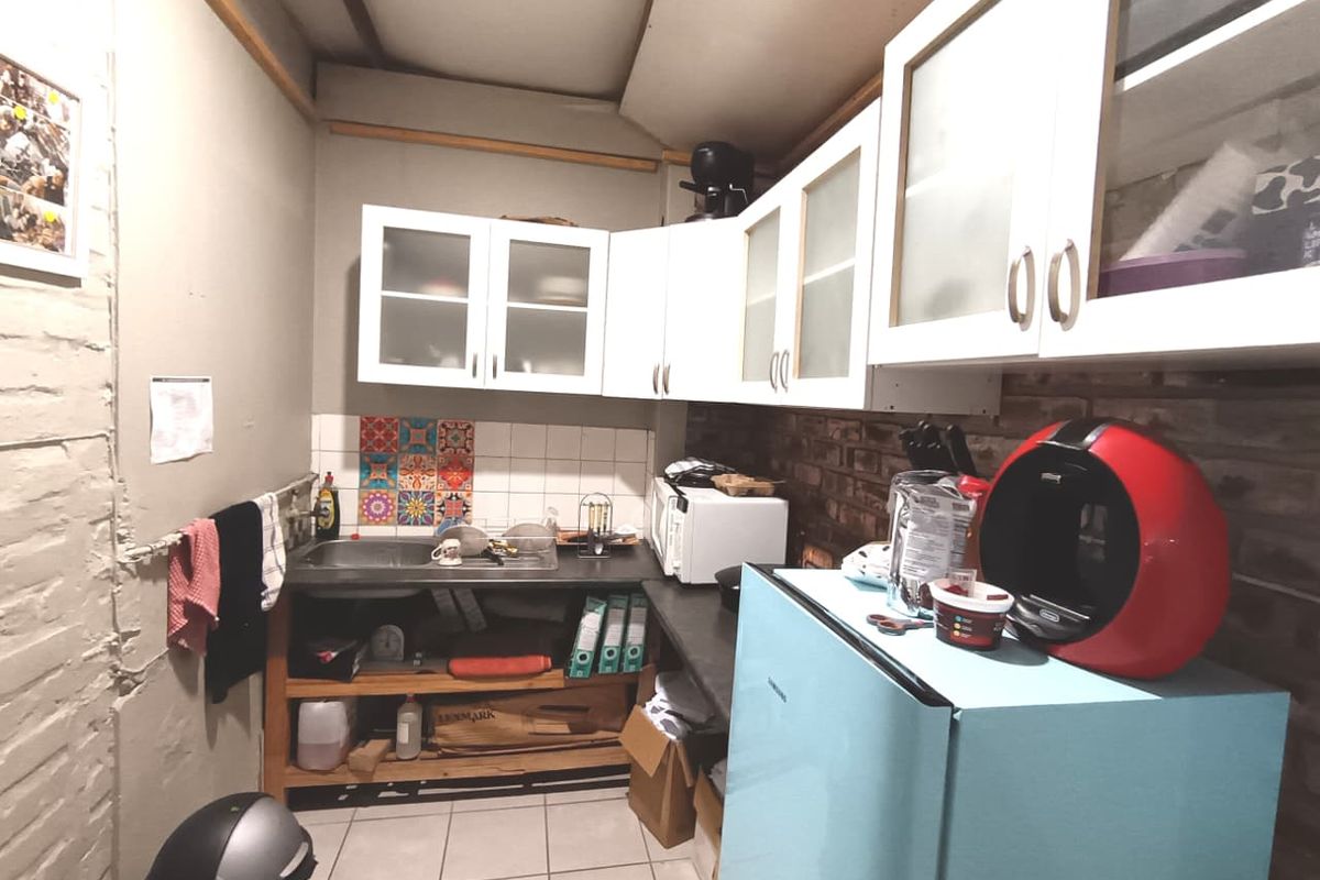 A compact kitchen area featuring built-in cabinetry, a stainless steel sink, tiled backsplash, and exposed brick wall elements, requiring cosmetic updates.