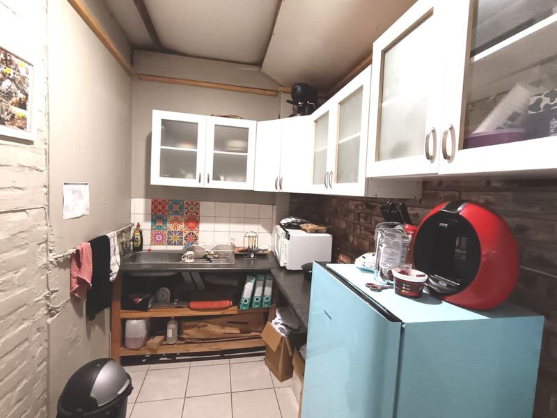 A compact kitchen area featuring built-in cabinetry, a stainless steel sink, tiled backsplash, and exposed brick wall elements, requiring cosmetic updates.