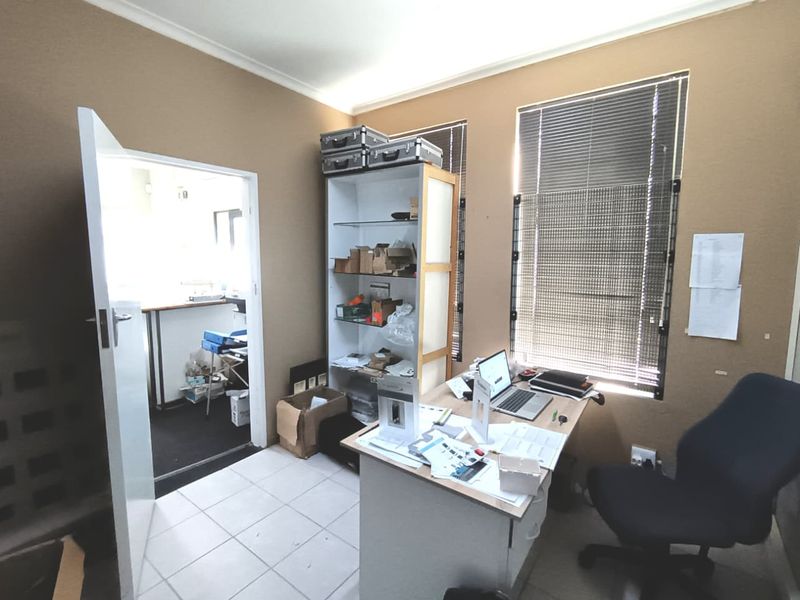 A functional commercial office space featuring tiled flooring, venetian blinds, and direct access to an adjacent utility area.