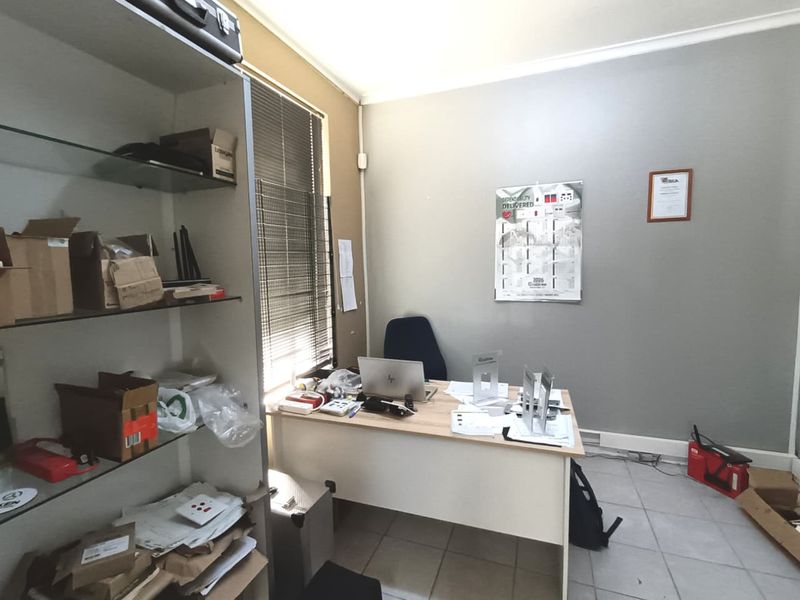 A functional commercial office space featuring tiled flooring, a built-in shelving unit, and venetian blinds, providing a practical environment for business operations.