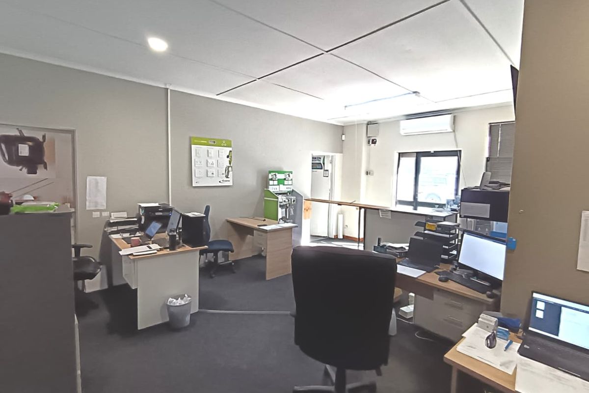 A functional commercial office space featuring carpeted flooring, a suspended ceiling, and a wall-mounted air conditioning unit.