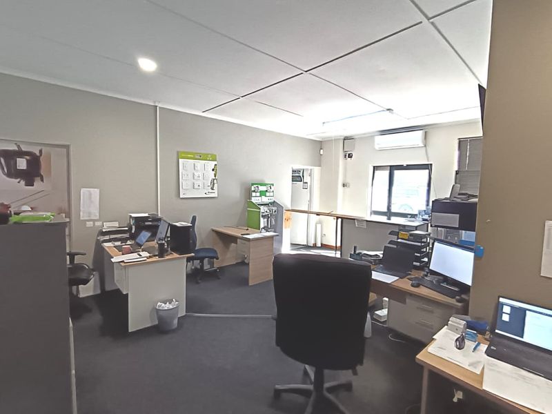 A functional commercial office space featuring carpeted flooring, a suspended ceiling, and a wall-mounted air conditioning unit.