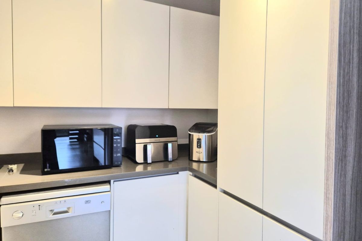 A modern kitchen featuring sleek white handleless cabinetry, stone countertops, and an integrated dishwasher, offering a clean and functional workspace.
