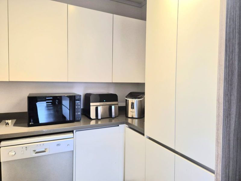 A modern kitchen featuring sleek white handleless cabinetry, stone countertops, and an integrated dishwasher, offering a clean and functional workspace.