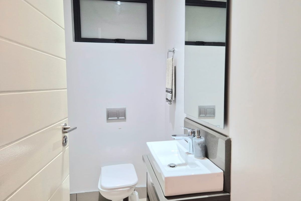 A modern, compact guest bathroom featuring a wall-hung toilet, vanity basin with mixer tap, and a large wall mirror.