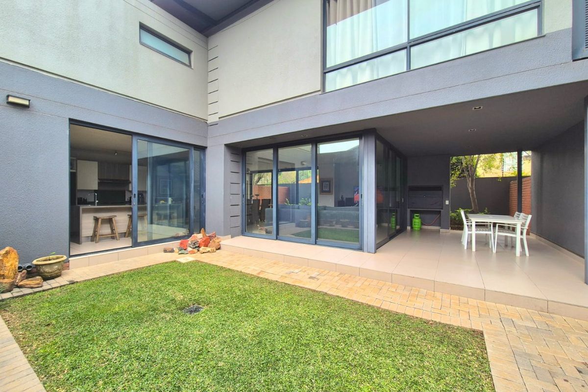 A modern rear exterior featuring a covered patio with a built-in braai, sliding glass doors leading to the interior, and a landscaped garden area.
