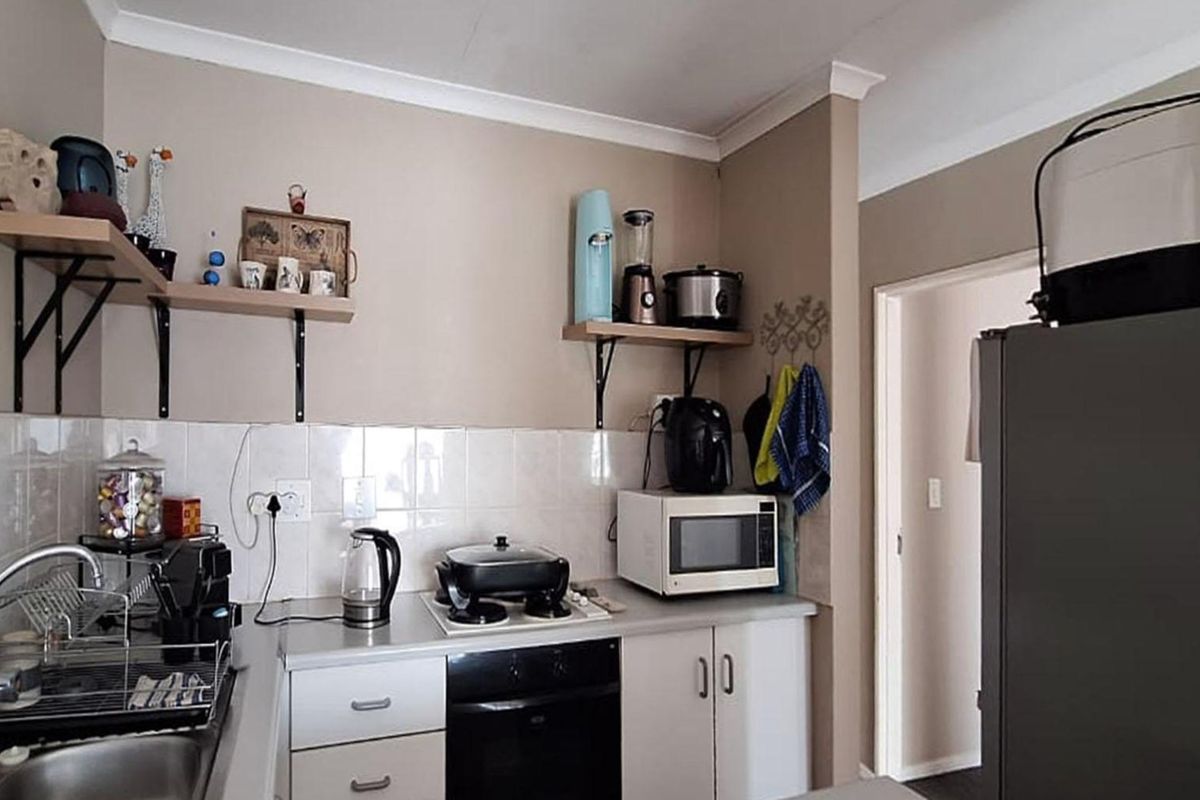 Compact kitchen featuring built-in cabinetry, a tiled backsplash, integrated oven and hob, and open shelving for additional storage.