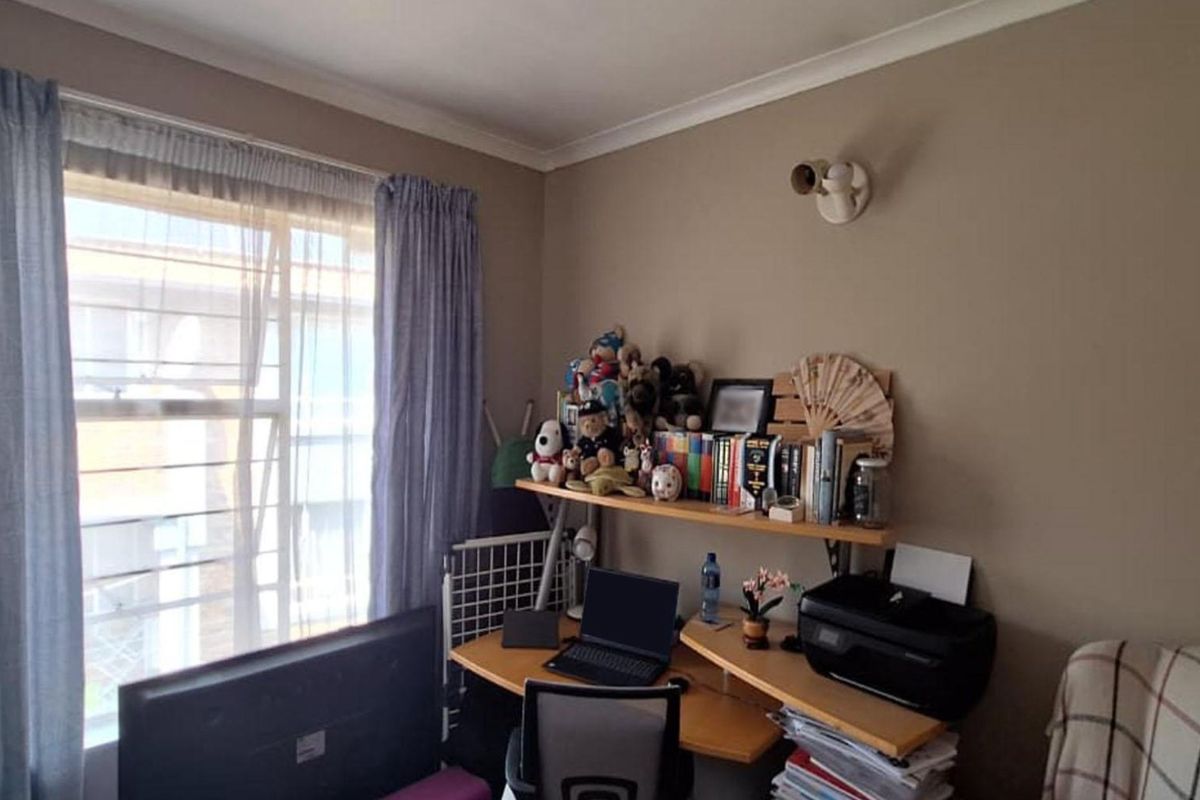 A functional bedroom or home office space featuring a window with curtain tracks and a wall-mounted light fixture.
