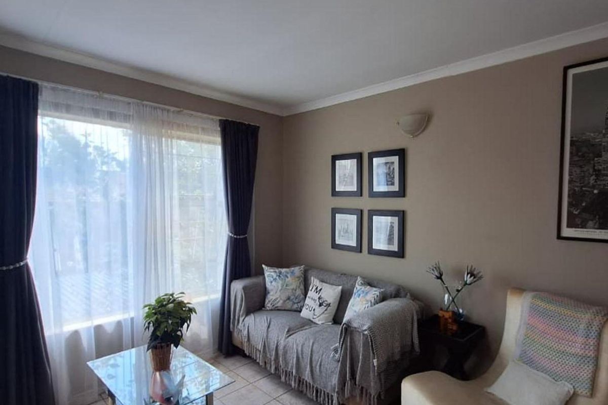 A cozy living room featuring tiled flooring, neutral wall tones, and a large window with curtains, providing natural light to the space.