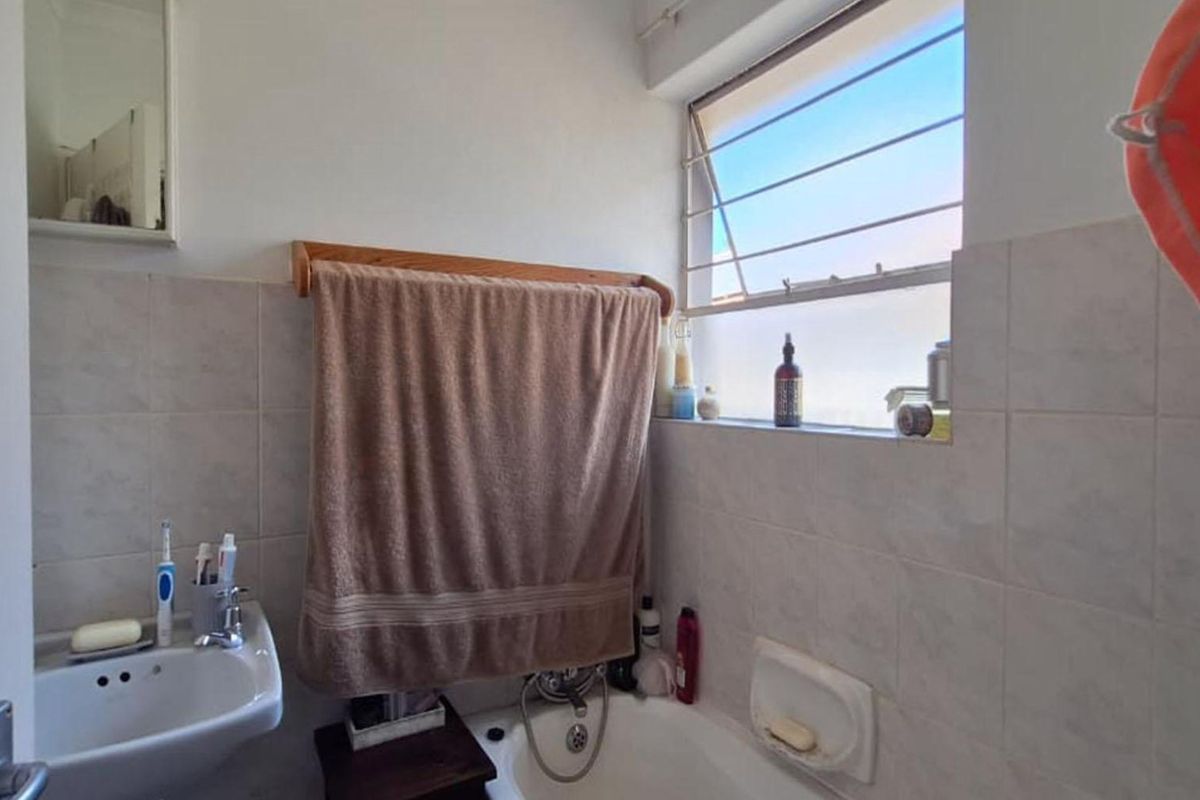 A functional bathroom featuring a wall-mounted basin, a bathtub with integrated shower fittings, and a frosted glass window for natural light and privacy.