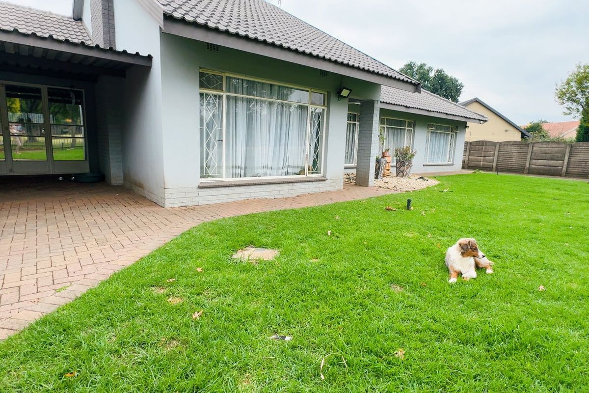 Rear view of the house featuring a paved patio area, large windows, and a well-maintained lawn enclosed by a concrete boundary wall.