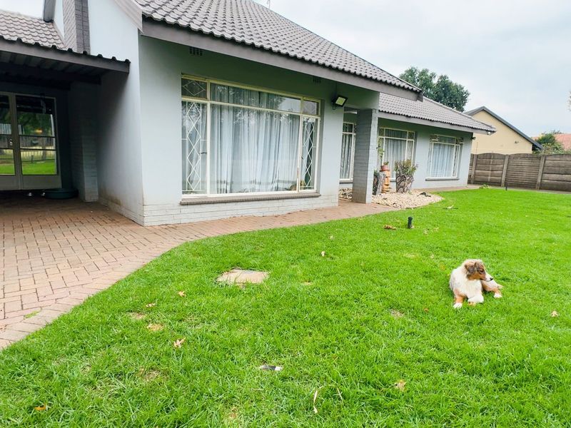 Rear view of the house featuring a paved patio area, large windows, and a well-maintained lawn enclosed by a concrete boundary wall.