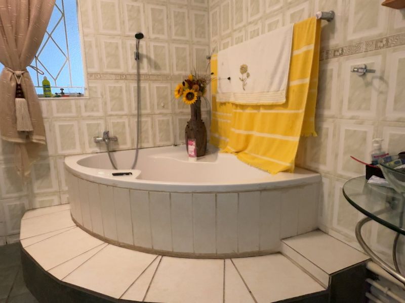 Bathroom featuring a corner bathtub with tiled surround, glass vessel sink, and full-height wall tiling.