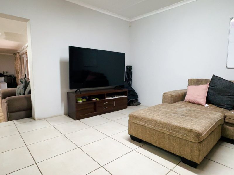 A living room featuring neutral tiled flooring and a coved ceiling, with an open-plan layout leading into an adjacent room.