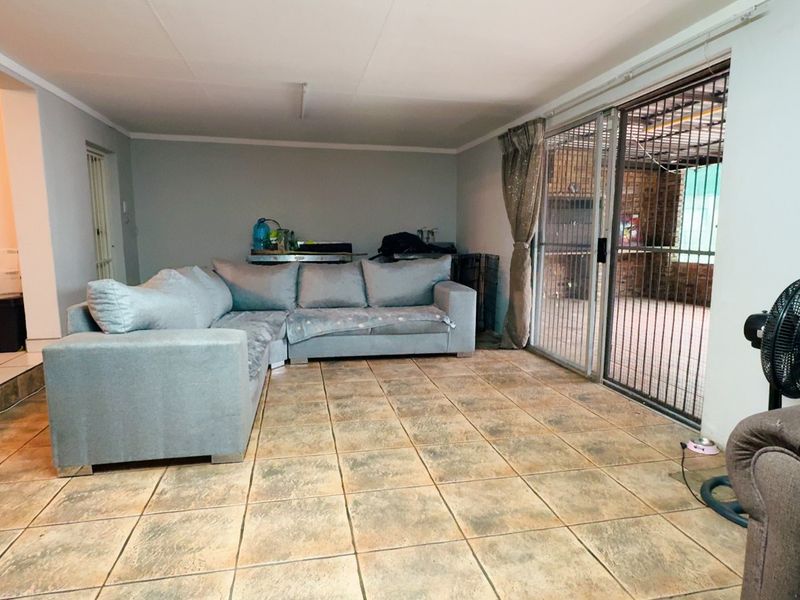 A living room featuring tiled flooring and a sliding glass door with a security gate, providing direct access to an outdoor area.