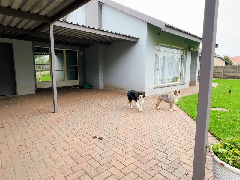 A covered paved patio area adjacent to the house, featuring a carport structure, sliding glass doors, and access to the rear garden.