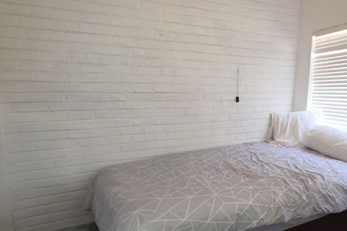 A bedroom featuring a white painted brick feature wall and fitted venetian blinds.