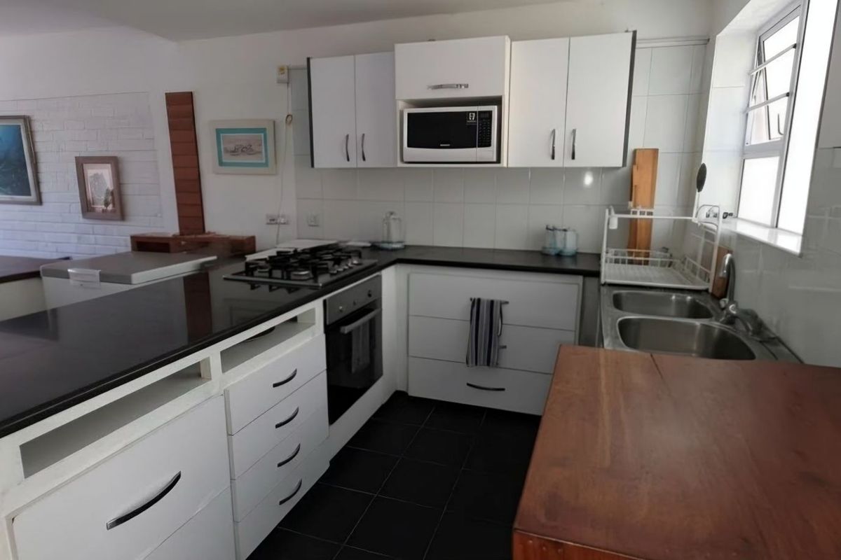 A functional kitchen featuring white cabinetry, black granite countertops, a gas hob, built-in oven, and a double sink with tiled backsplash.