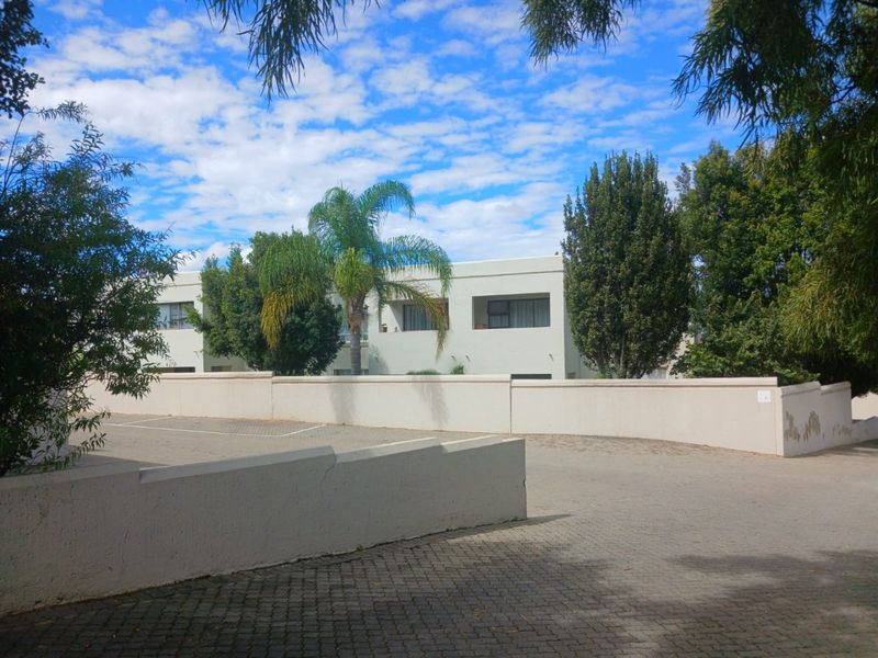 Exterior view of an apartment complex featuring a paved driveway and boundary wall with mature landscaping.