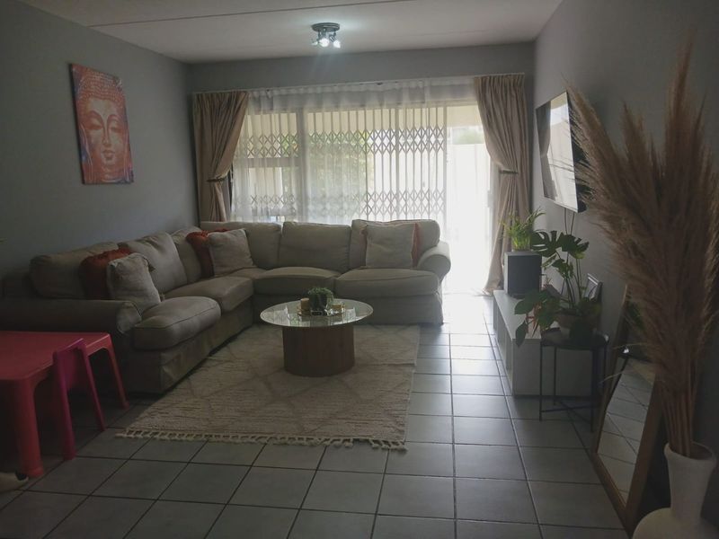 A comfortable living room featuring tiled flooring and a sliding glass door with security gate, providing access to the outdoor area.