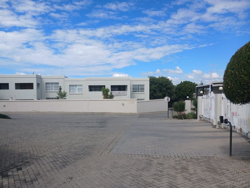 Front exterior view of the apartment complex featuring a paved driveway, perimeter wall, and secure gated entrance.