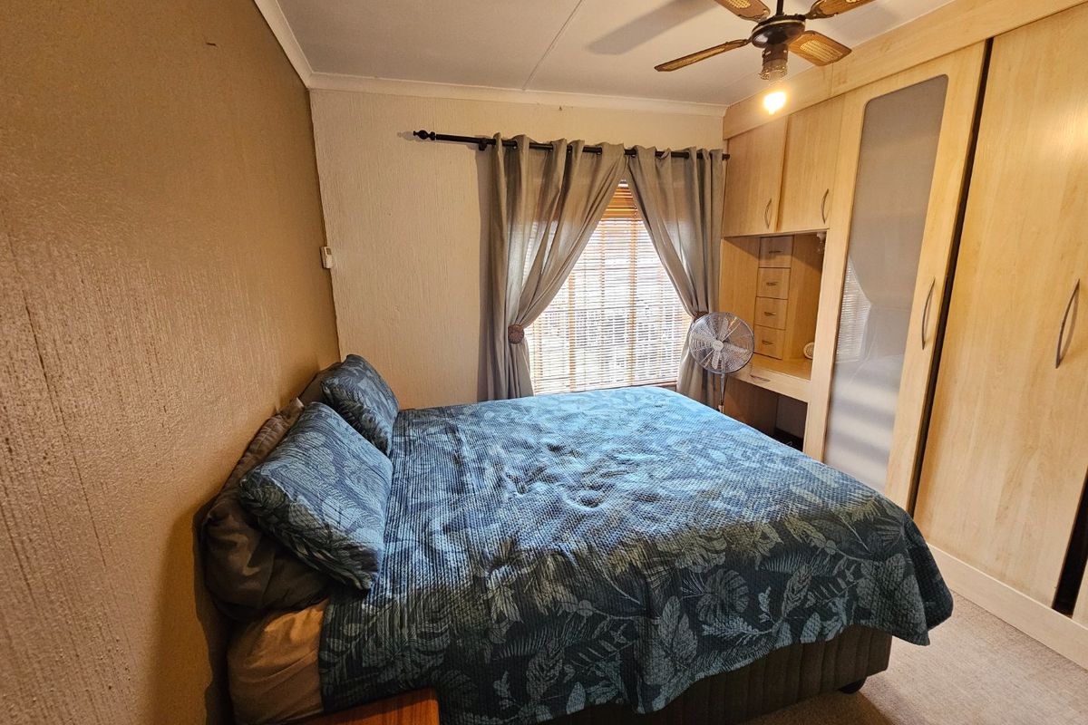 A functional bedroom featuring built-in wooden cupboards with an integrated vanity area and a ceiling fan.