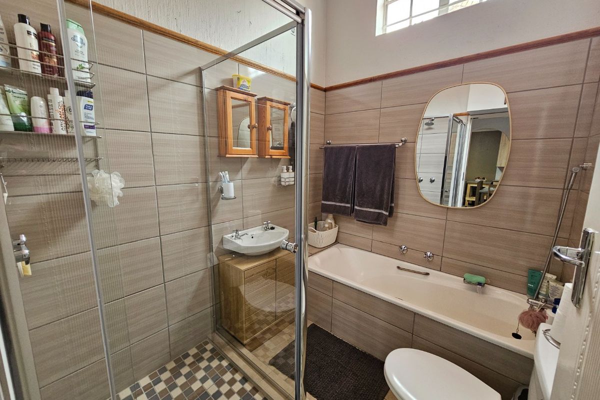 A functional bathroom featuring a glass shower enclosure, a built-in vanity with basin, a bathtub, and neutral wall tiling.